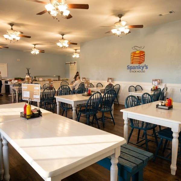 Bright, spacious dining room at Spanky's Stack House with light blue walls, white tables, and teal chairs.